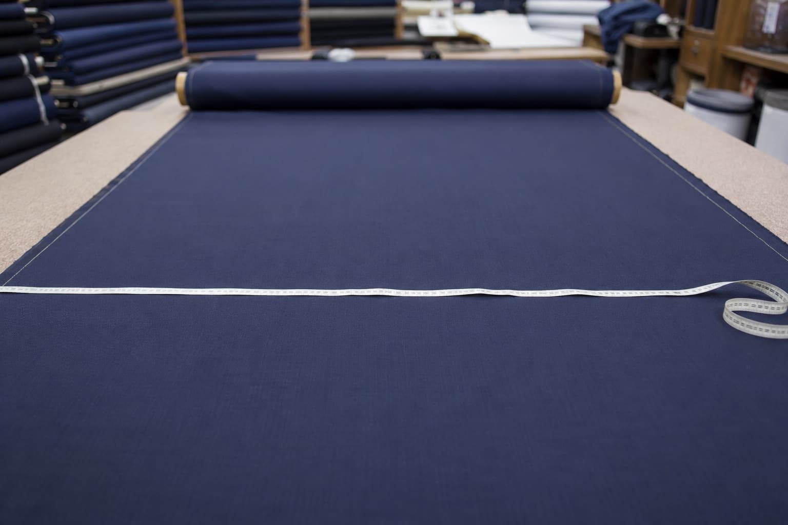 Fabric width being measured with a tape across an unrolled navy suiting roll on a cutting table