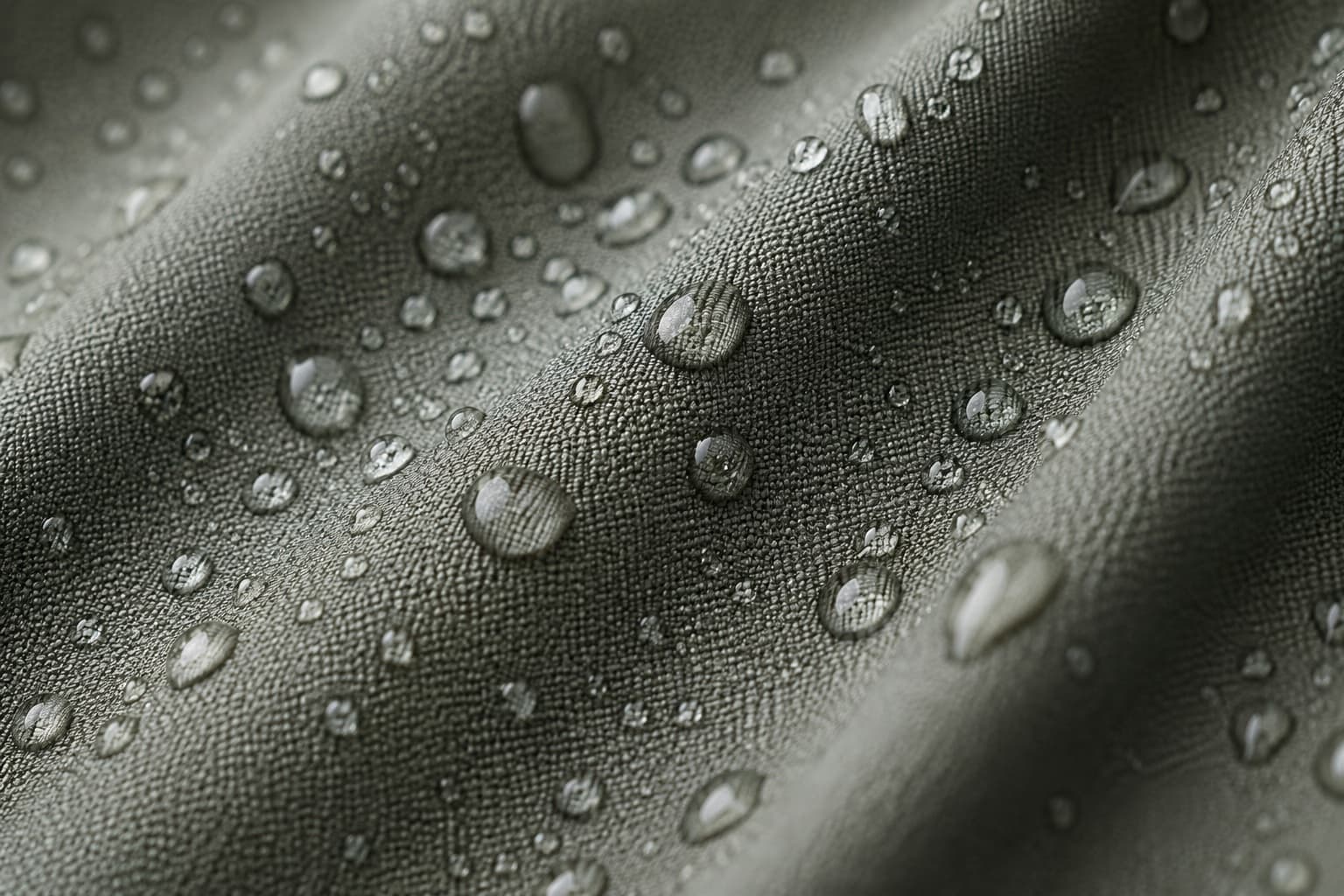 Close-up of water beading on grey-green uniform fabric, showing a moisture-control finish