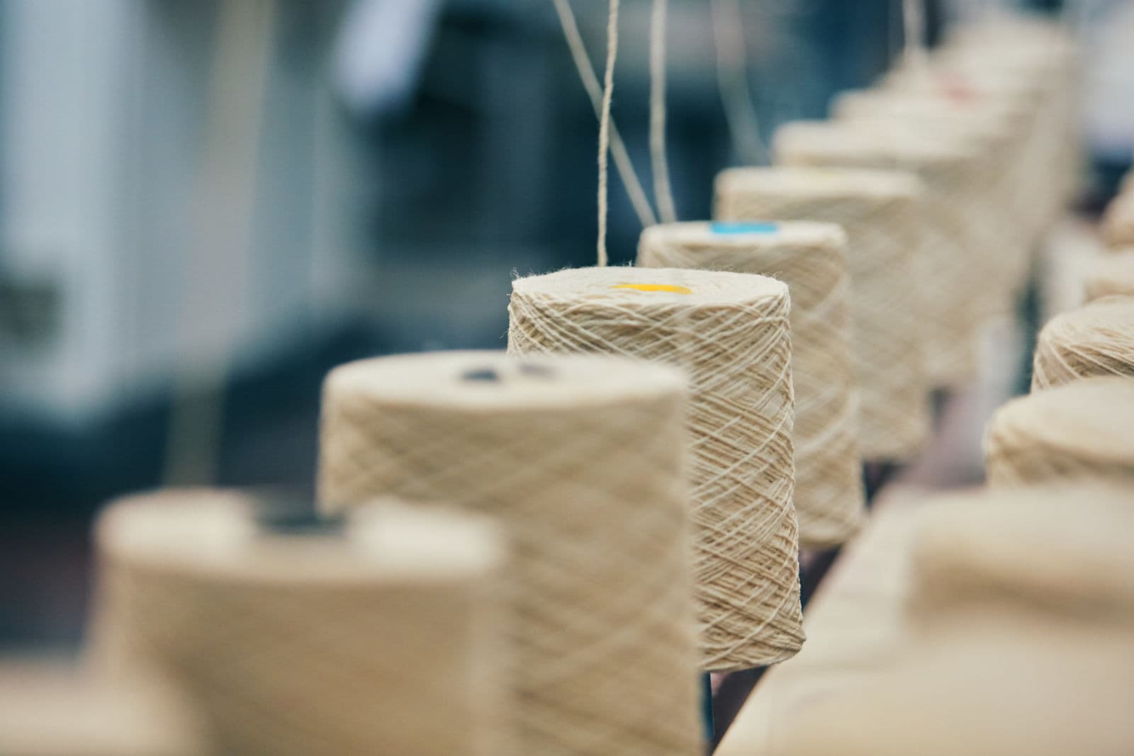 Rows of spun yarn cones on a spinning frame, showing the fine twisted threads used to weave uniform fabric