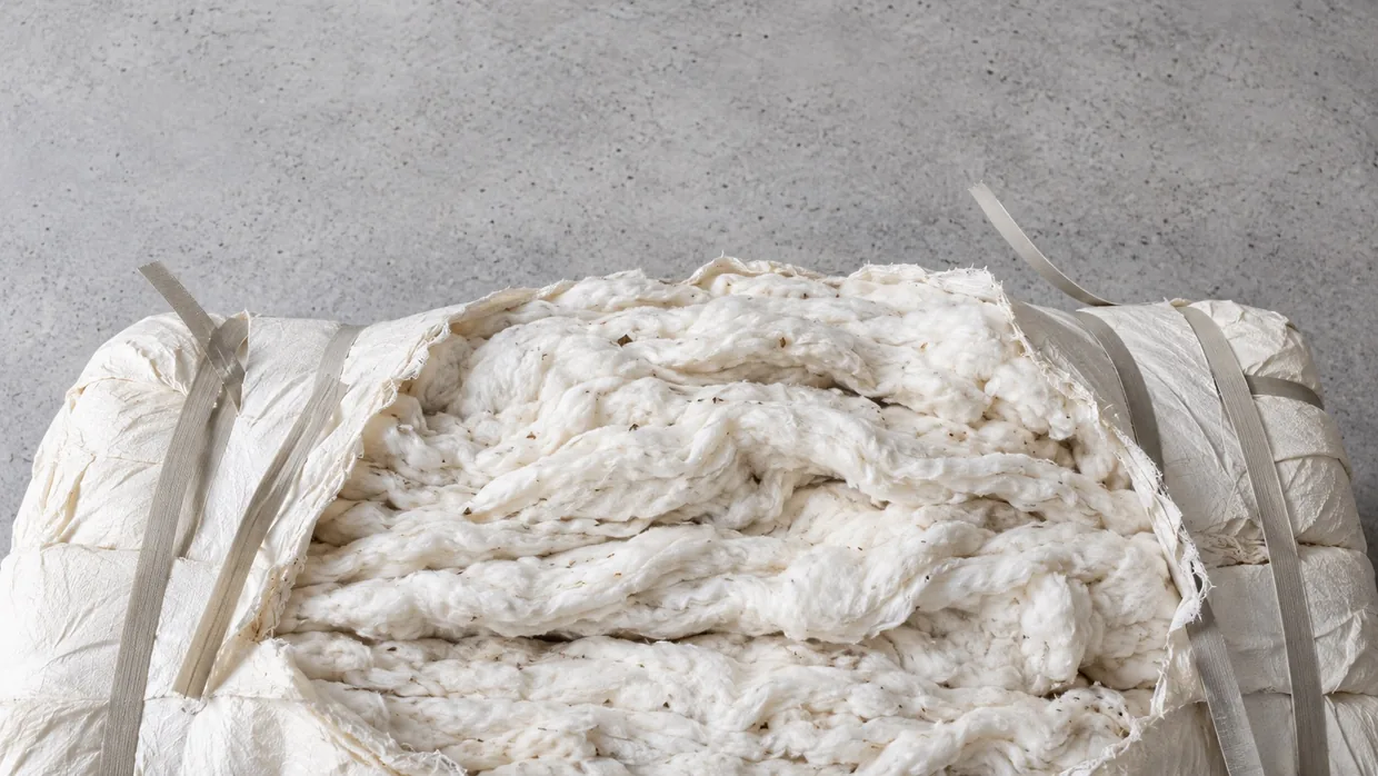 A single compressed cotton bale with its strapping cut open, showing layered white lint, on a clean concrete floor in soft daylight