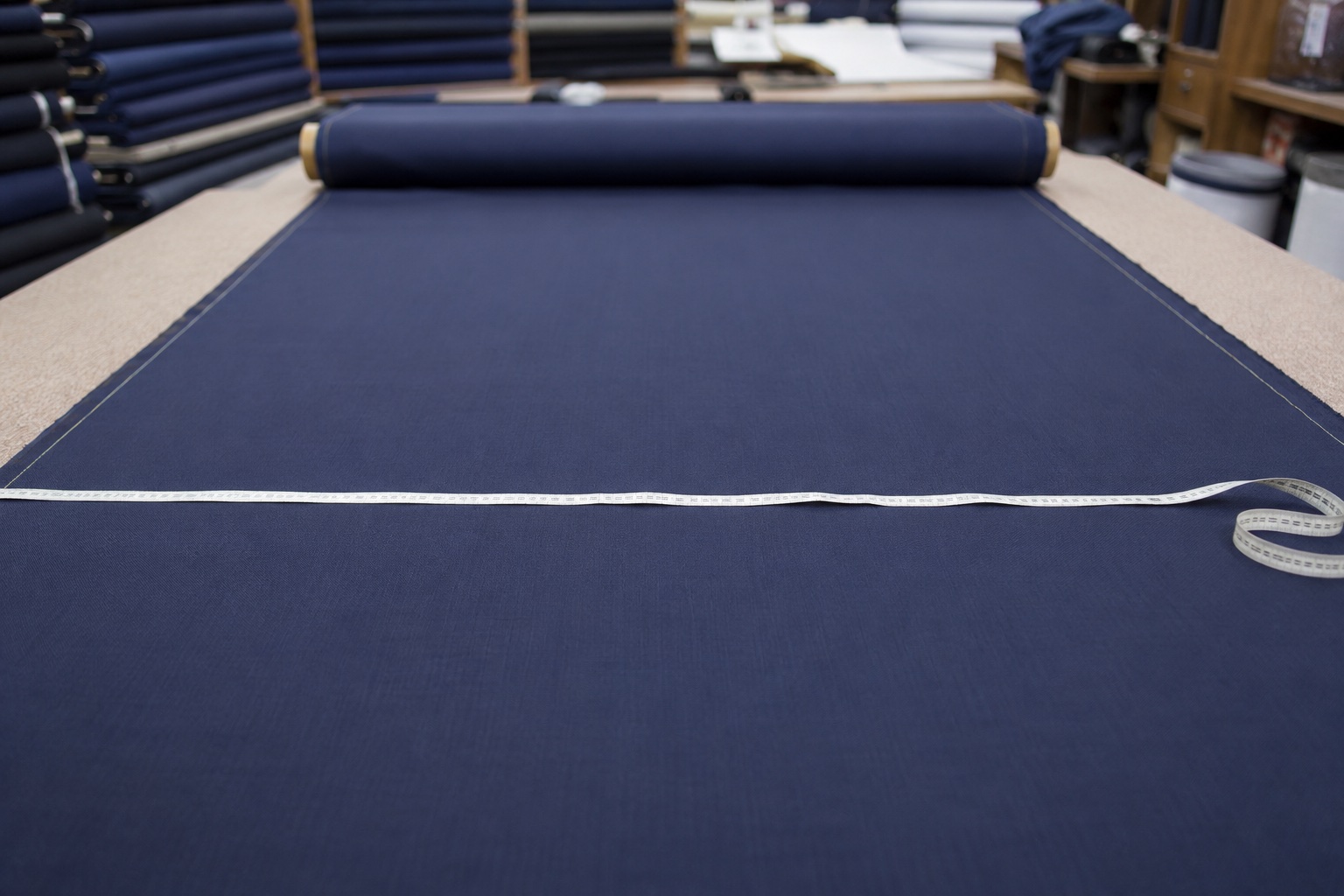 Fabric width being measured with a tape across an unrolled navy suiting roll on a cutting table